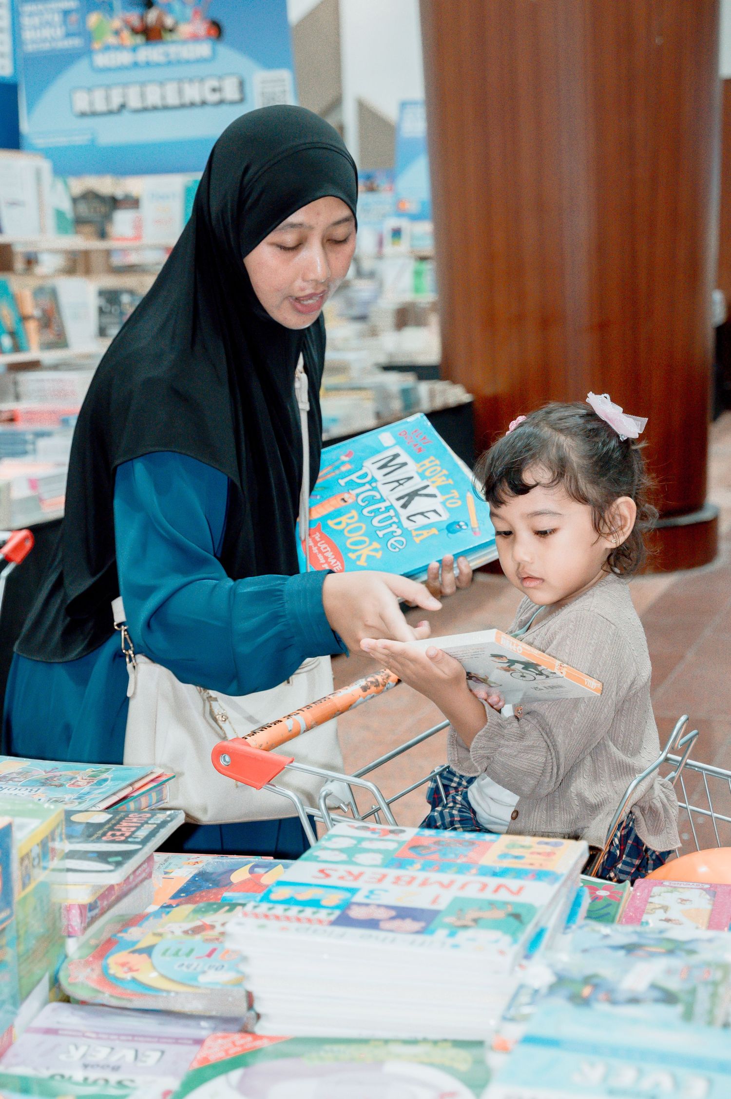 Woman in hijab and young child browsing colorful books at a bookstore display table together.