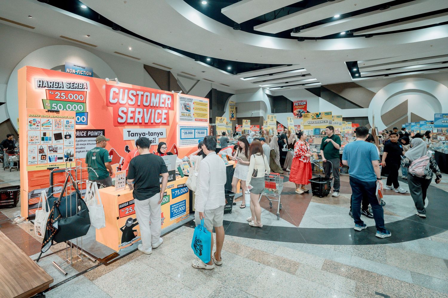 Busy customer service booth at a shopping mall event with crowds of people browsing products and signage.