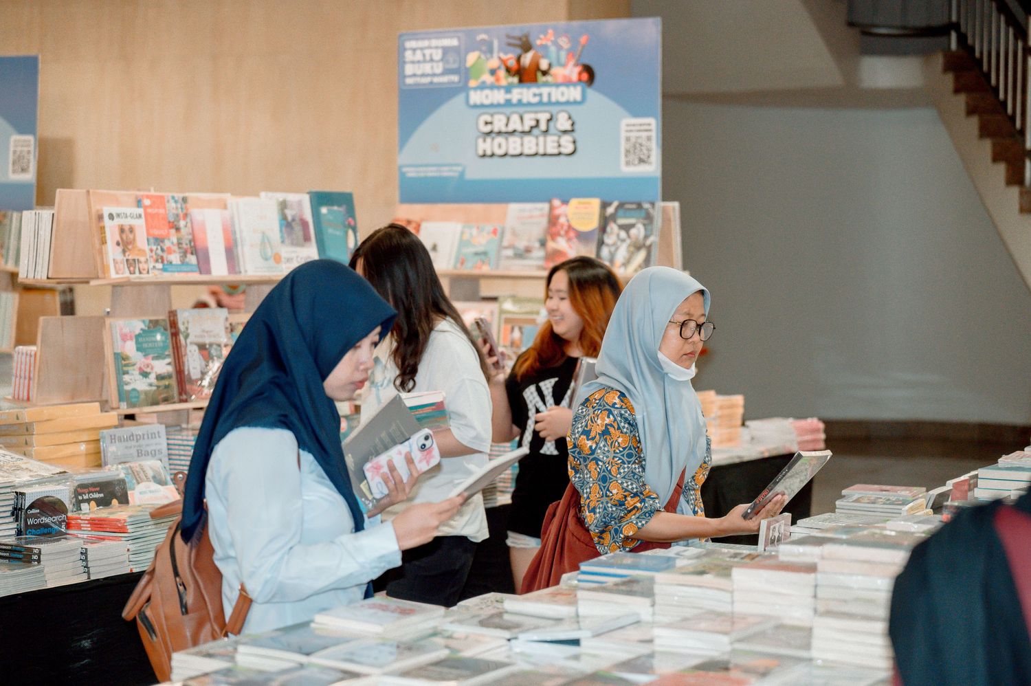Women in hijabs browsing books at a non-fiction craft and hobbies bookstore display table.