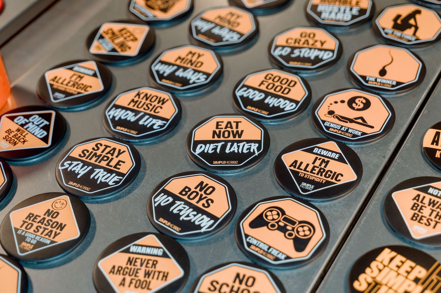 Collection of round black and orange novelty buttons with humorous sayings like Eat Now Diet Later and No Boys Yes Video Games.