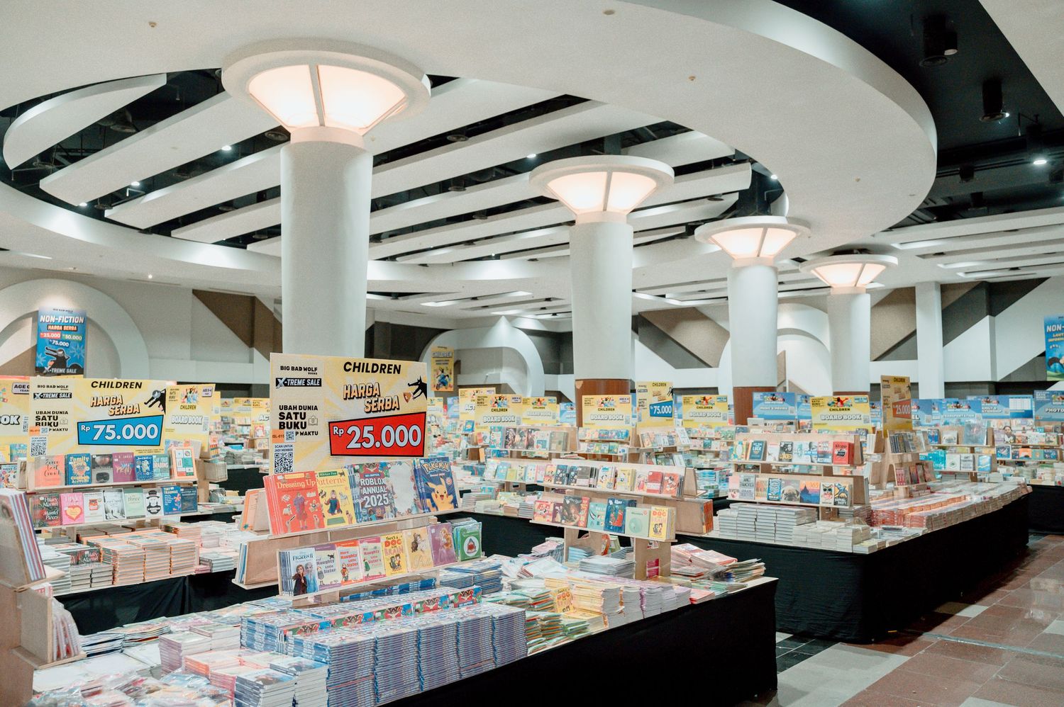 Interior of a large bookstore with white columns, bright lighting, and colorful book displays with price signs in Japanese.