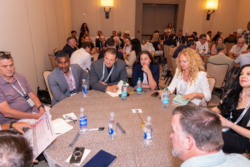 Business professionals networking at round tables during a corporate conference event in a hotel ballroom.