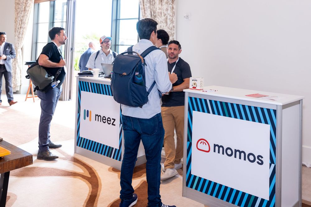 Professionals networking at a conference near Meez and Momos branded booths in a bright event venue.