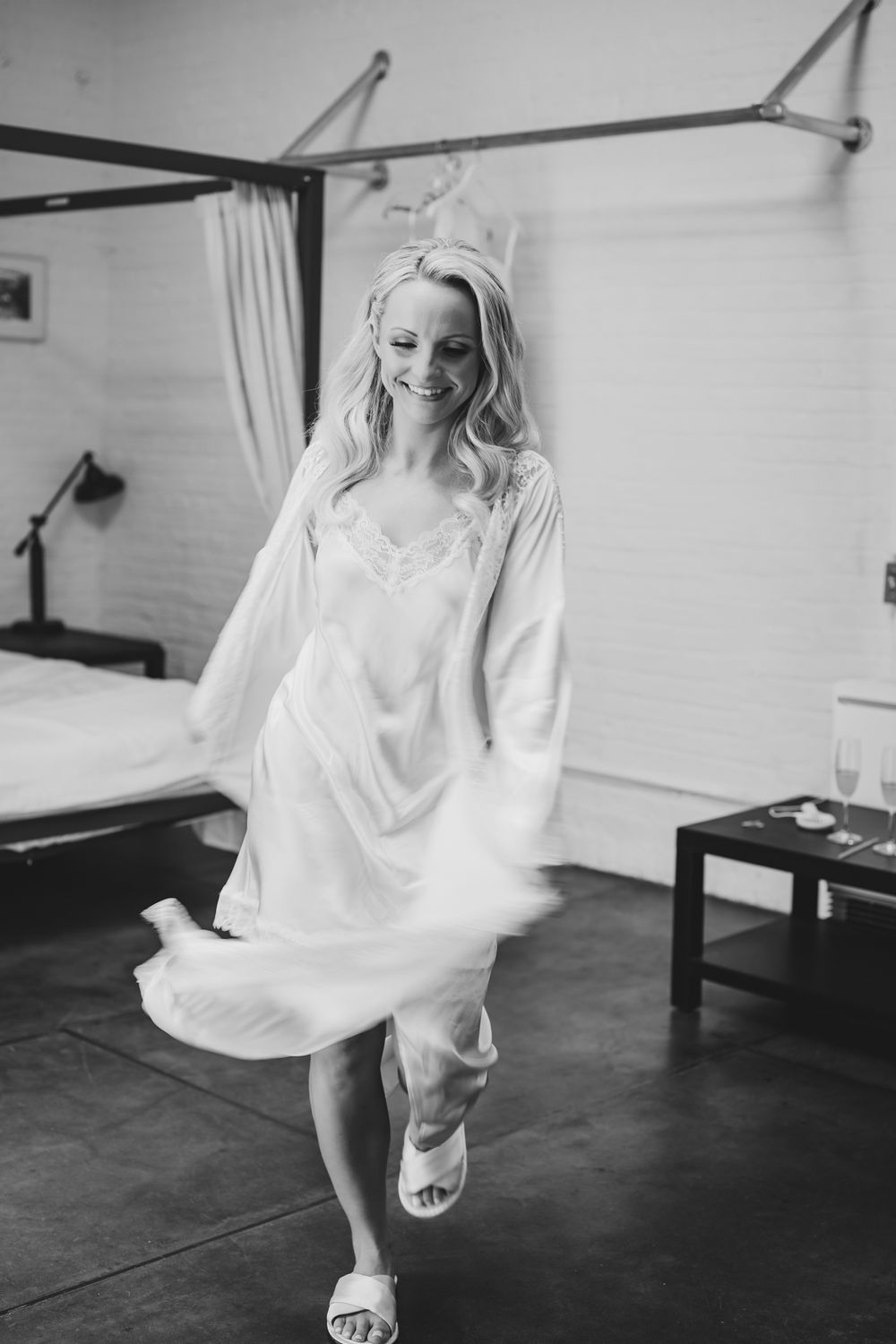 Smiling bride twirling in white robe and slip dress in black and white wedding preparation photo.