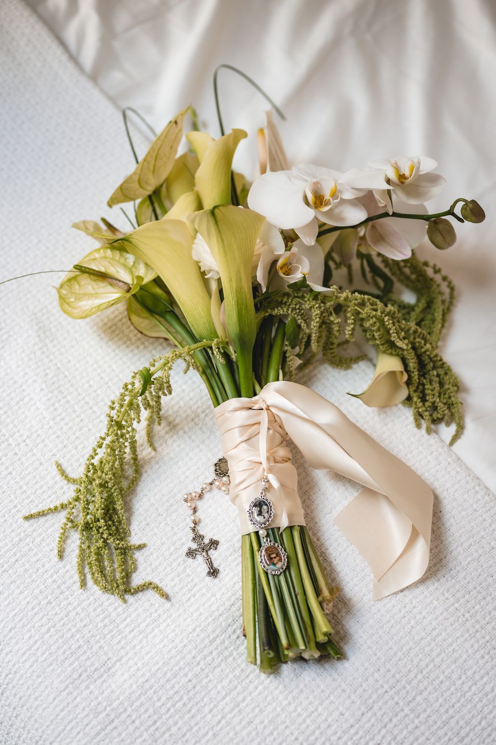 Elegant bridal bouquet with white orchids, yellow calla lilies, and greenery tied with champagne ribbon and cross charm.