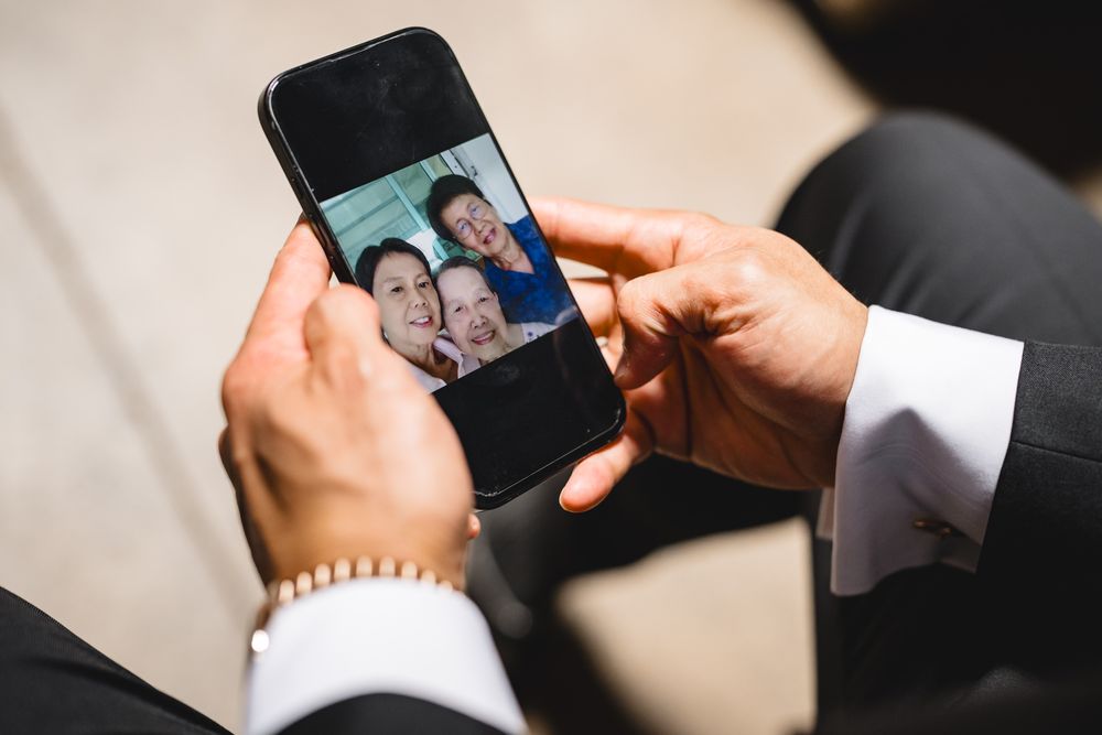 Groom in suit holds smartphone displaying video call with smiling family members on wedding day.