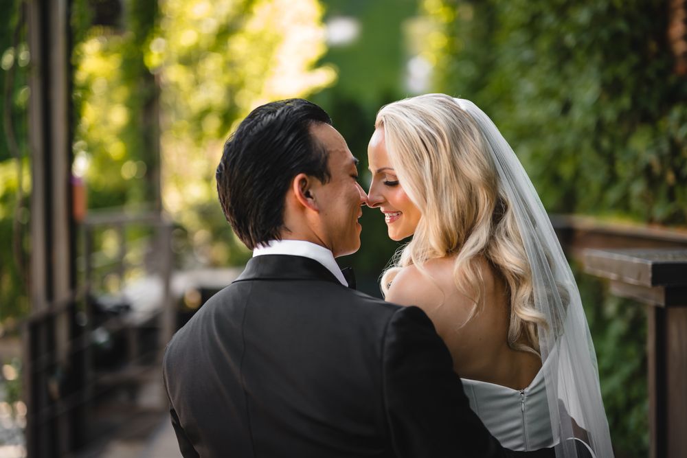 Bride and groom share a romantic moment outdoors, with the blonde bride in a veil smiling at her partner.