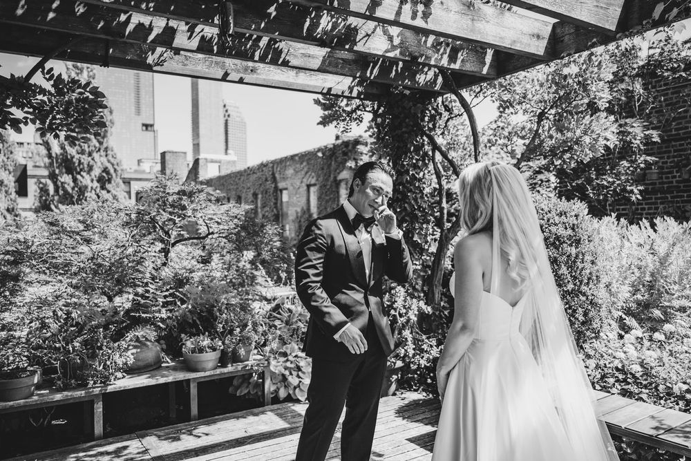 Black and white photo of groom reacting emotionally during first look with bride in lush garden wedding venue.