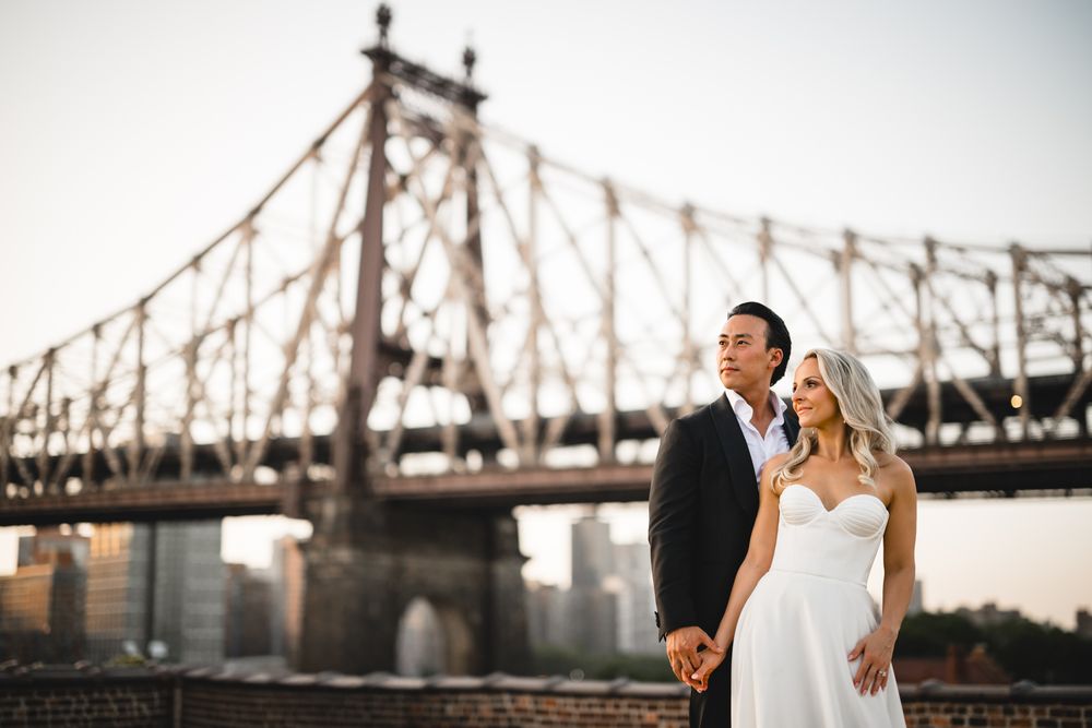 Bride and groom hold hands with iconic Queensboro Bridge at sunset in the background in New York City.