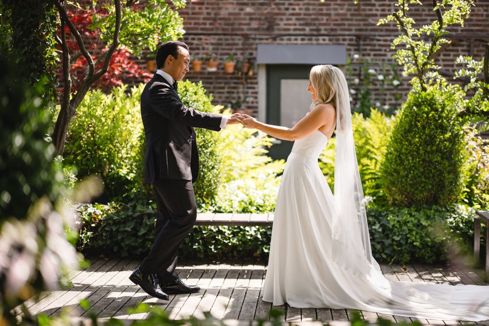 A bride and groom hold hands in a lush garden courtyard, sharing a romantic moment on their wedding day.