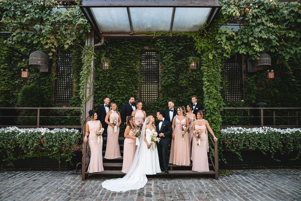 Wedding party poses before an ivy-covered building facade on cobblestone street.