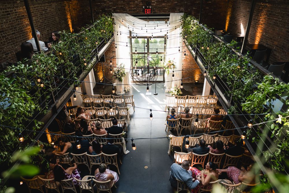 Aerial view of elegant wedding ceremony in brick venue with string lights and lush greenery.