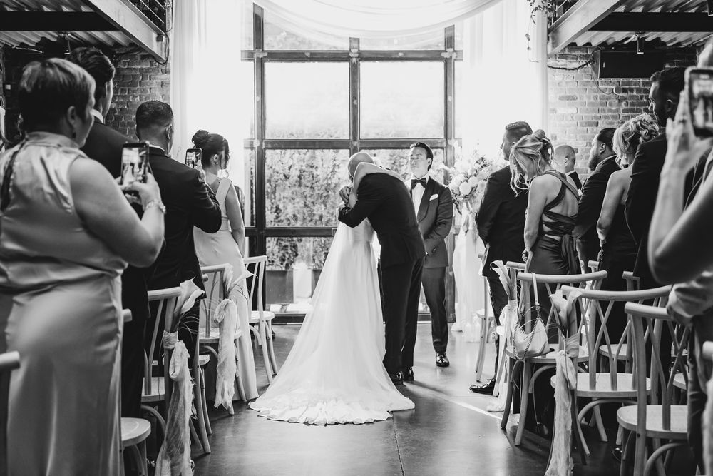 Groom kisses bride at the altar during indoor wedding ceremony in black and white.