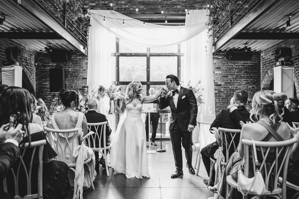 Black and white photo of a bride and groom sharing a joyful moment at their indoor wedding ceremony with brick walls.