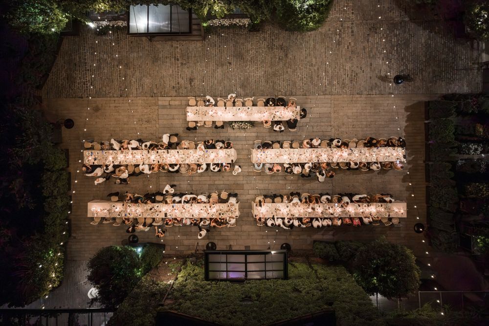 Aerial night view of illuminated long banquet tables arranged in rows at an outdoor wedding reception.