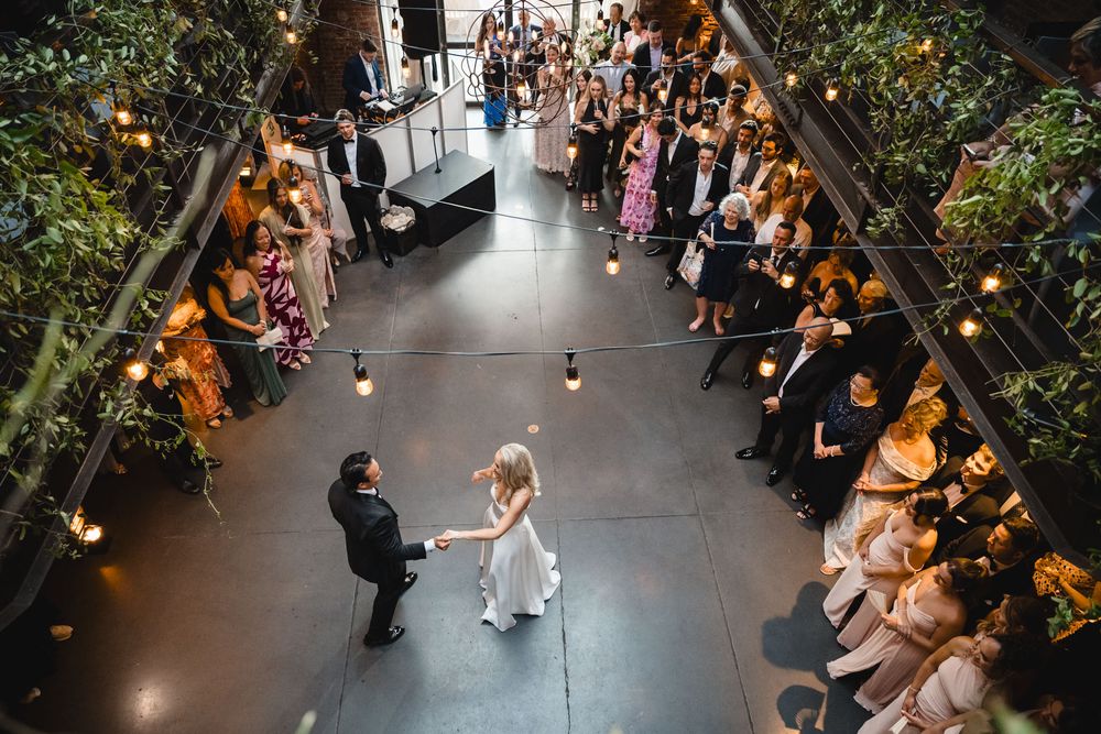 Aerial view of bride and groom sharing first dance surrounded by guests at an indoor wedding venue.