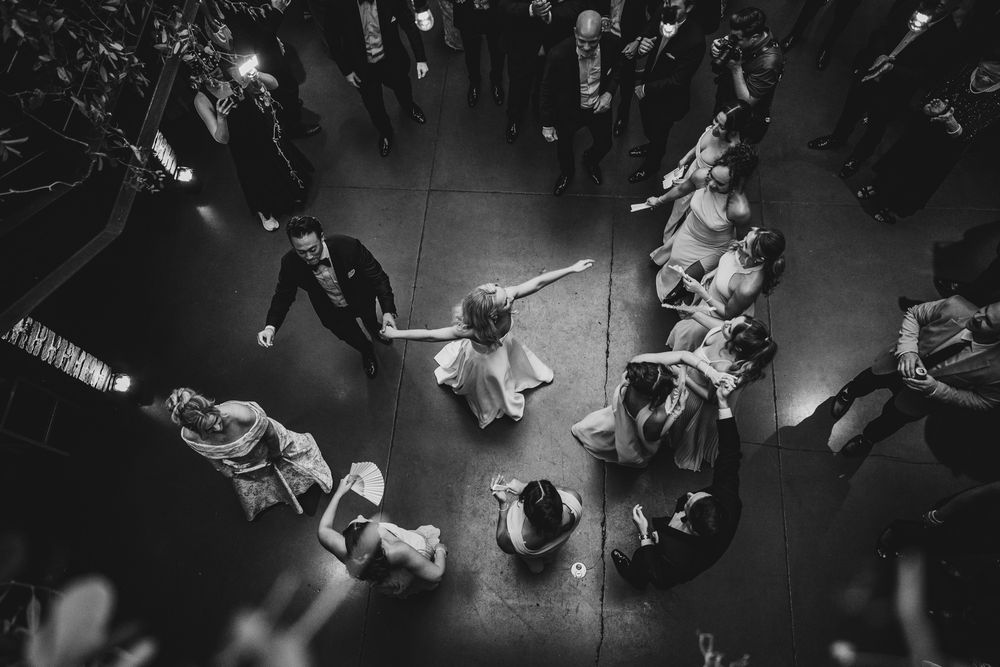 Aerial black and white photo of wedding guests forming a circle on the dance floor during a reception.