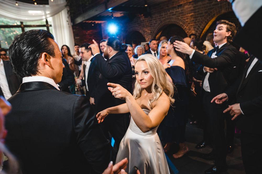 Bride in white gown dancing joyfully with guests at elegant wedding reception venue.