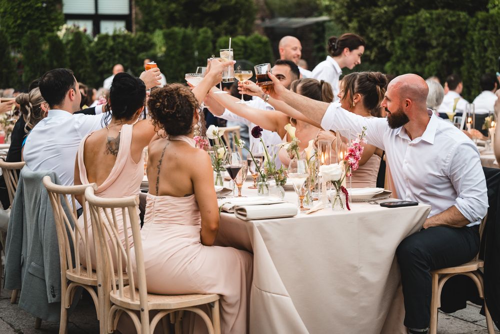 Wedding guests raising glasses in a toast at an elegant outdoor reception dinner table.