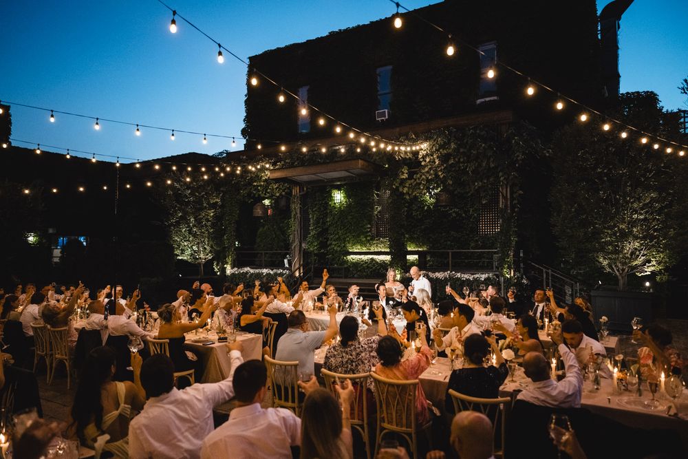 Elegant outdoor wedding reception at night with string lights illuminating guests seated at round tables.