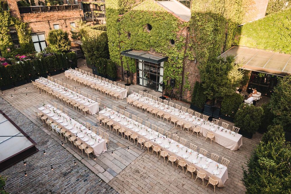 Aerial view of elegant outdoor wedding reception with long banquet tables set in a brick courtyard surrounded by lush greenery.