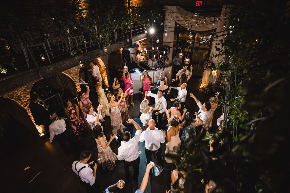Aerial view of wedding guests dancing outdoors at a night reception venue with string lights.