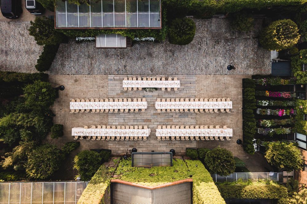 Aerial view of elegant outdoor wedding venue with rows of white chairs and tables surrounded by lush greenery.