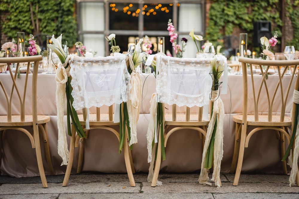 Elegant outdoor wedding reception with gold Chiavari chairs adorned with white lace and ribbon florals at a decorated table.