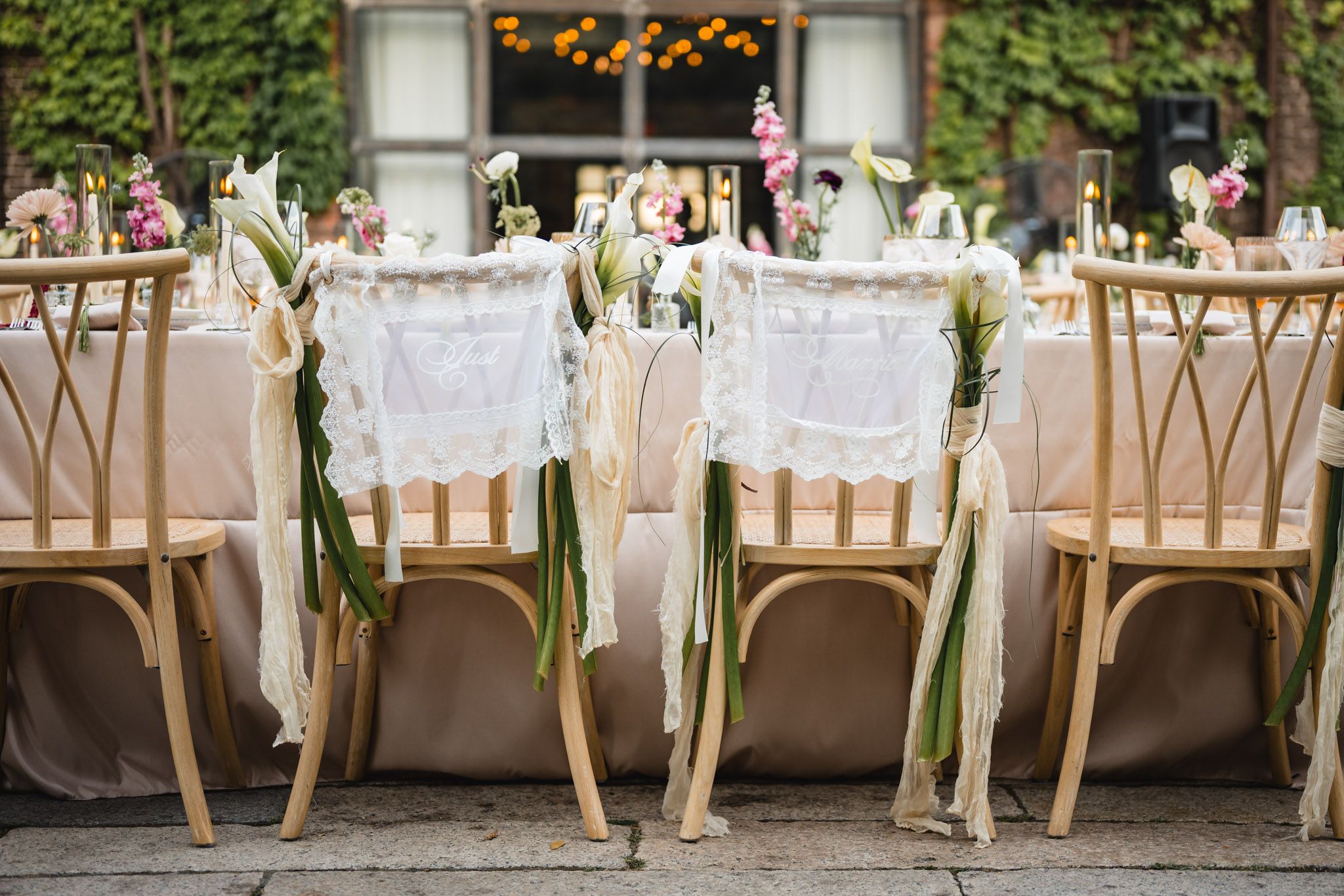 Elegant outdoor wedding reception with gold Chiavari chairs adorned with white lace and ribbon florals at a decorated table.