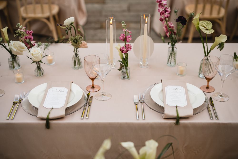 Elegant wedding reception table setting with blush linens, white plates, pink florals, and glowing candles.