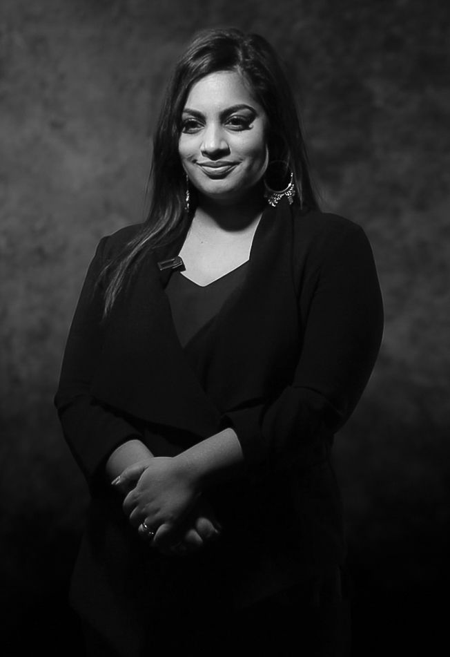 Black and white professional portrait of a smiling woman in a black blazer with hands clasped.