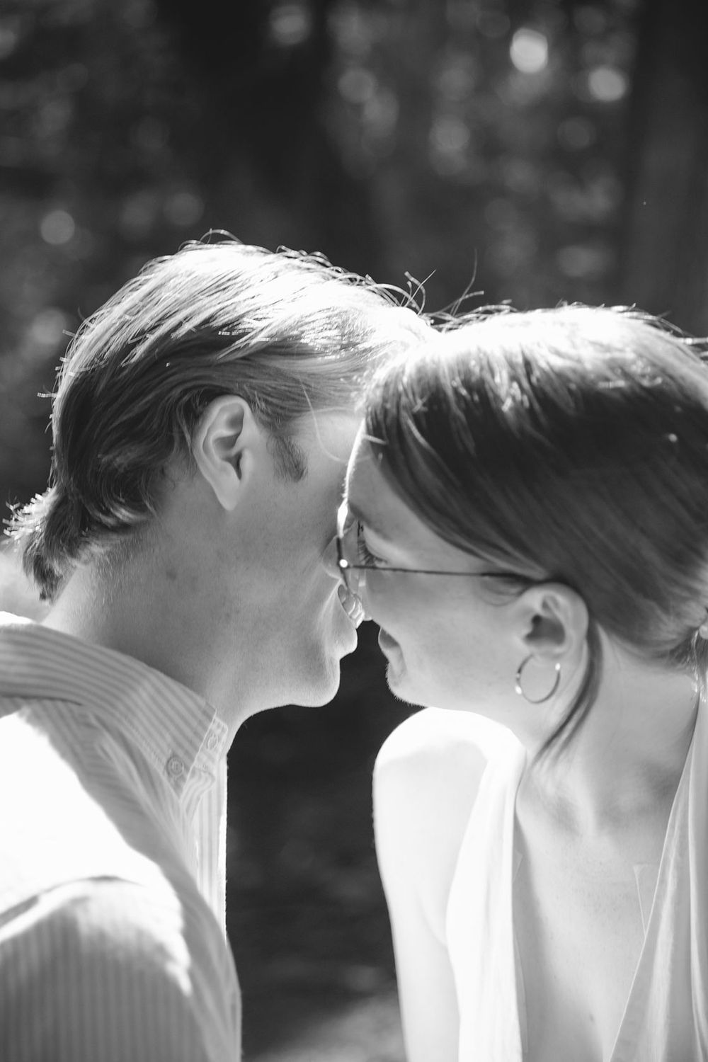 Black and white photo of a couple sharing a tender moment, leaning in for a kiss outdoors.