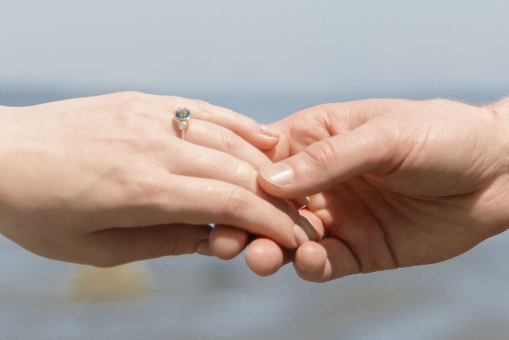 Close-up of two hands touching, woman wearing an elegant engagement ring, romantic proposal moment outdoors.