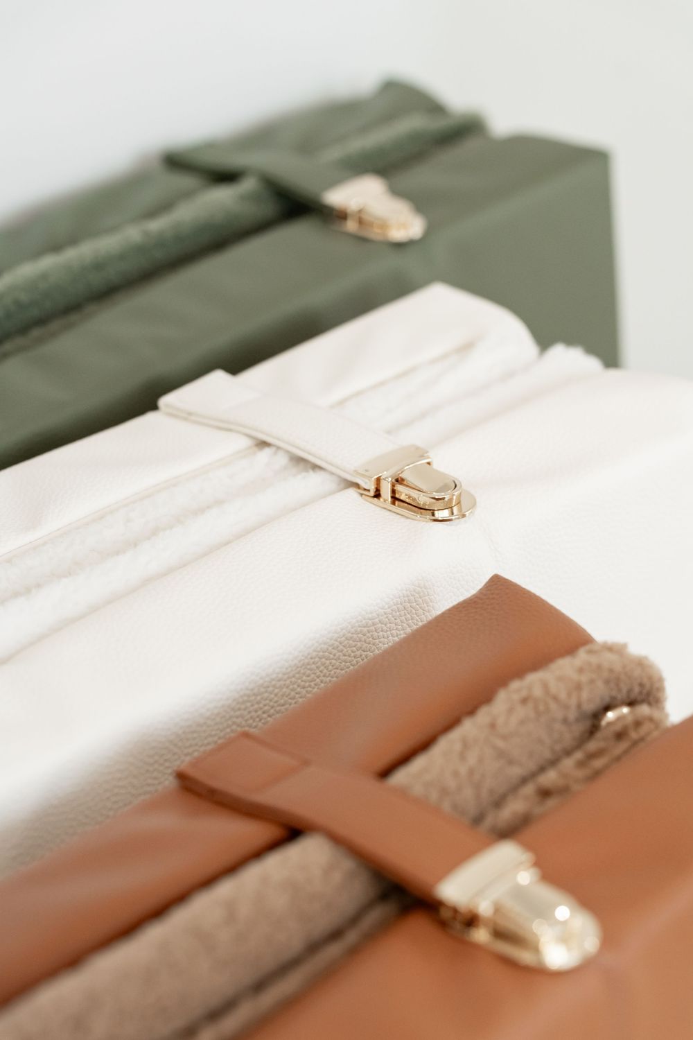 Three stacked handbags in olive green, cream, and tan leather with gold hardware closures on a white background.