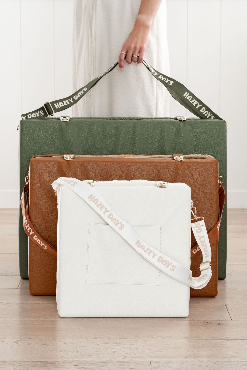 Three Hazy Days branded bags in olive green, tan, and white displayed against a white wall.