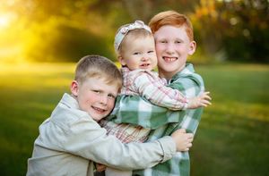 Two young siblings share a playful embrace while smiling outdoors in warm golden sunlight.