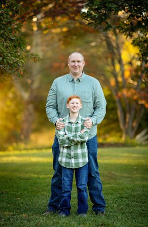 A pair in matching mint green shirts stand together on grass with golden autumn trees in the background.