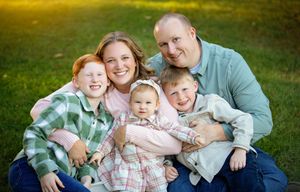 A group photo session in a grassy outdoor setting with coordinated casual outfits in soft colors.
