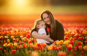Mother and daughter embracing in a vibrant tulip field at golden sunset, girl holding a red tulip.
