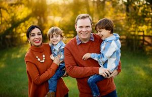 A family wearing coordinated rust-colored sweaters shares joyful moments together in a sunlit autumn field.
