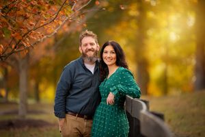 A couple embraces outdoors during golden hour autumn photography session with warm fall foliage in background.
