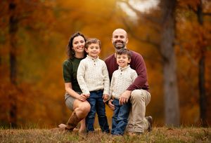 Family enjoying autumn afternoon together on fallen leaves in a park during golden hour.