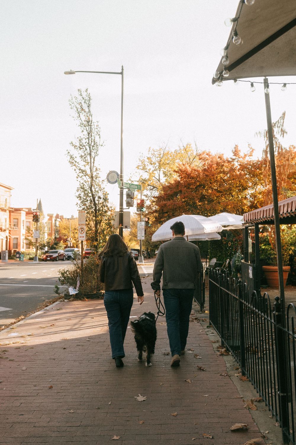 People walking along an autumn sidewalk with fall foliage and iron railings.