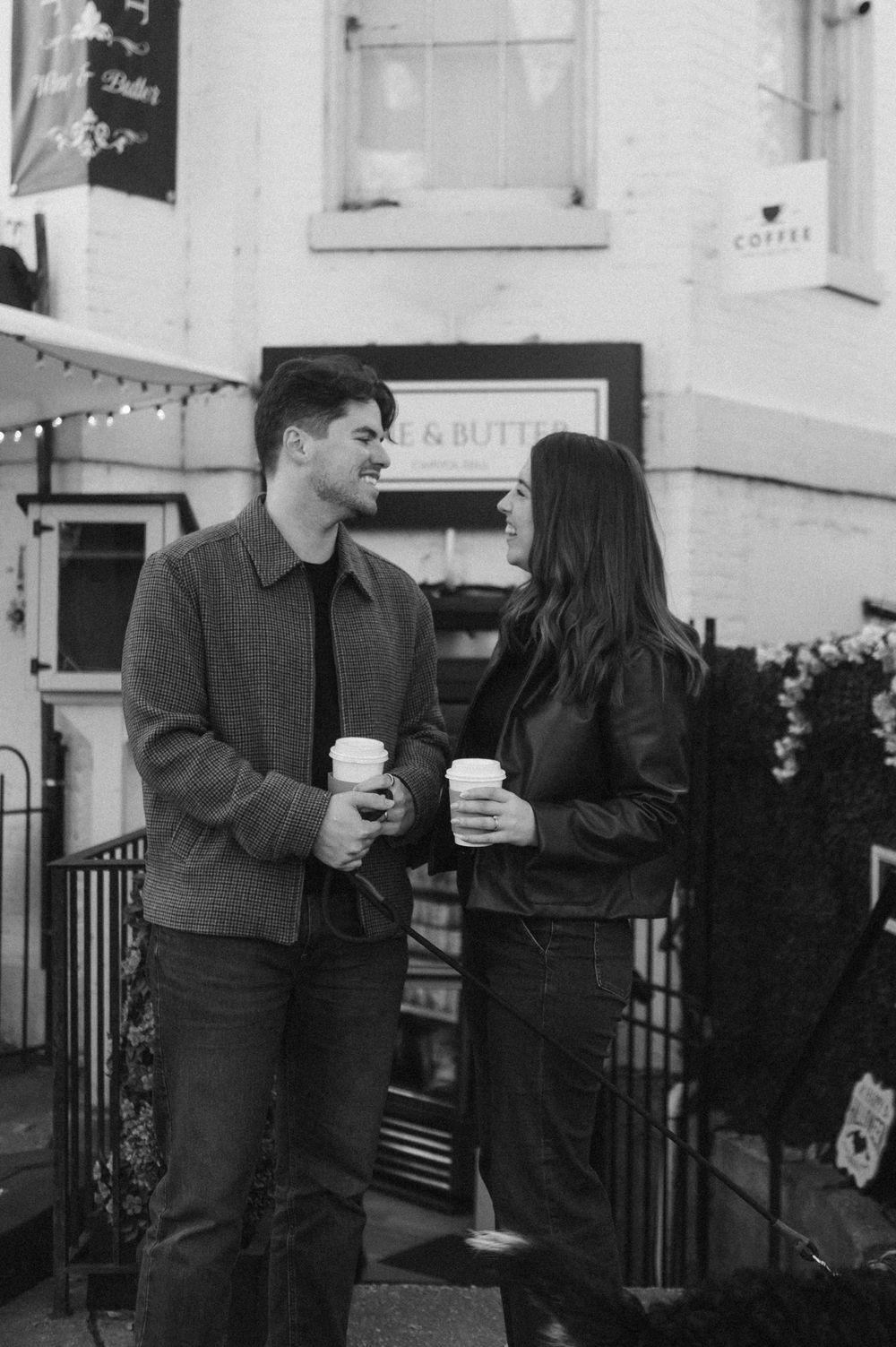Black and white photo of a couple sharing coffee outside a storefront.