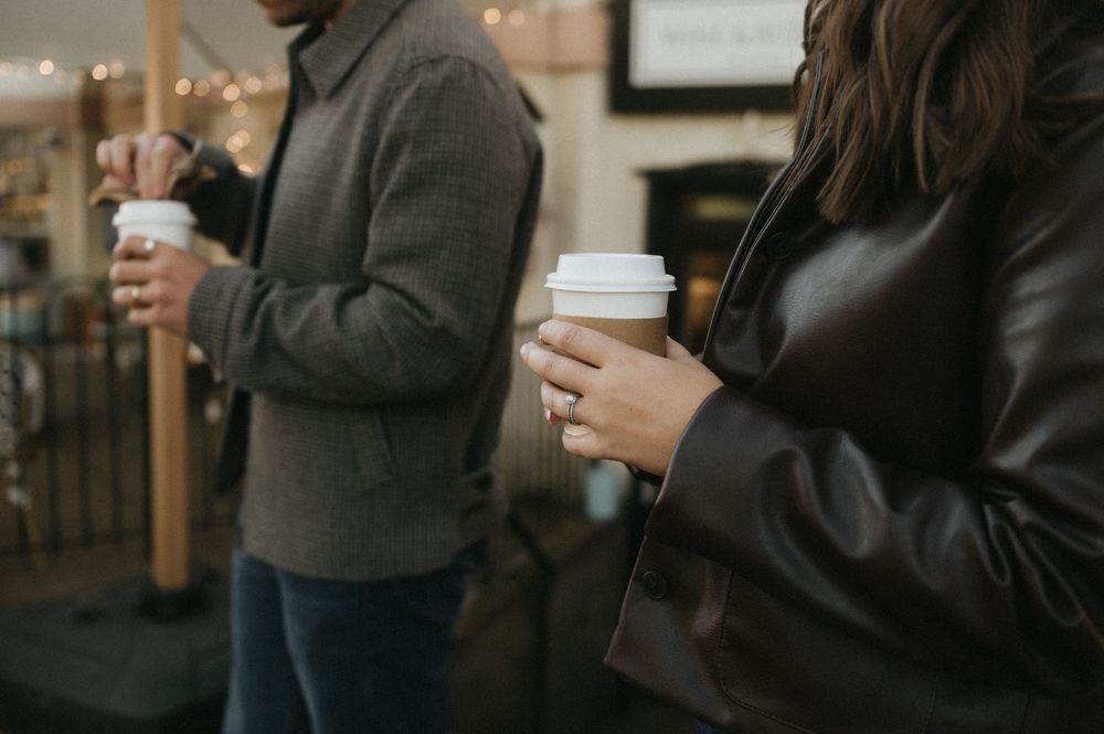 People in dark clothing holding coffee cups while having a casual conversation indoors.