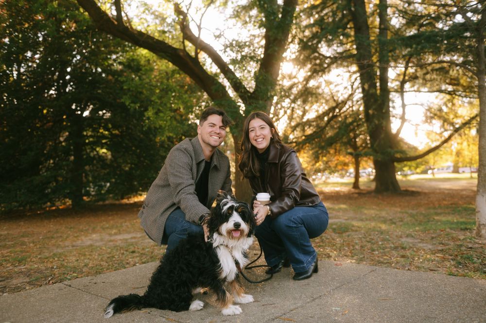 Couple crouching with their dog in a park during golden hour sunset.