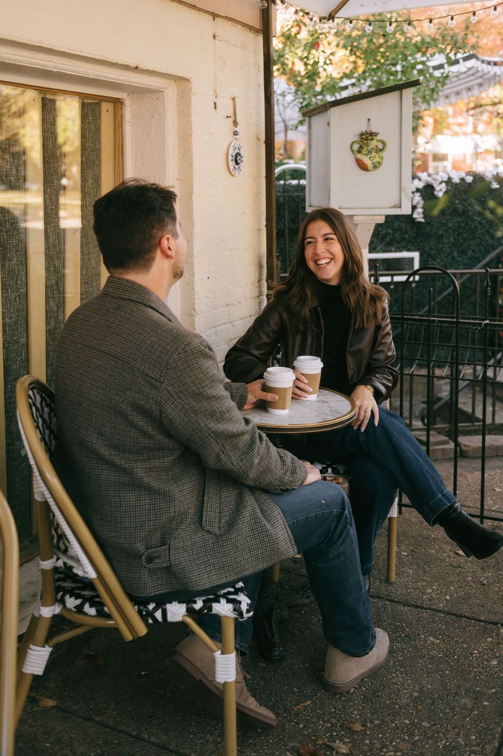 A couple enjoying coffee and conversation on a cozy outdoor patio with string lights overhead.