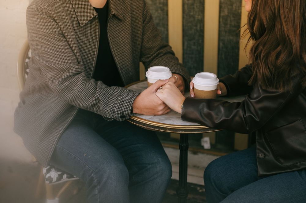 Coffee cups and hands shown during casual conversation at a dimly lit cafe table.
