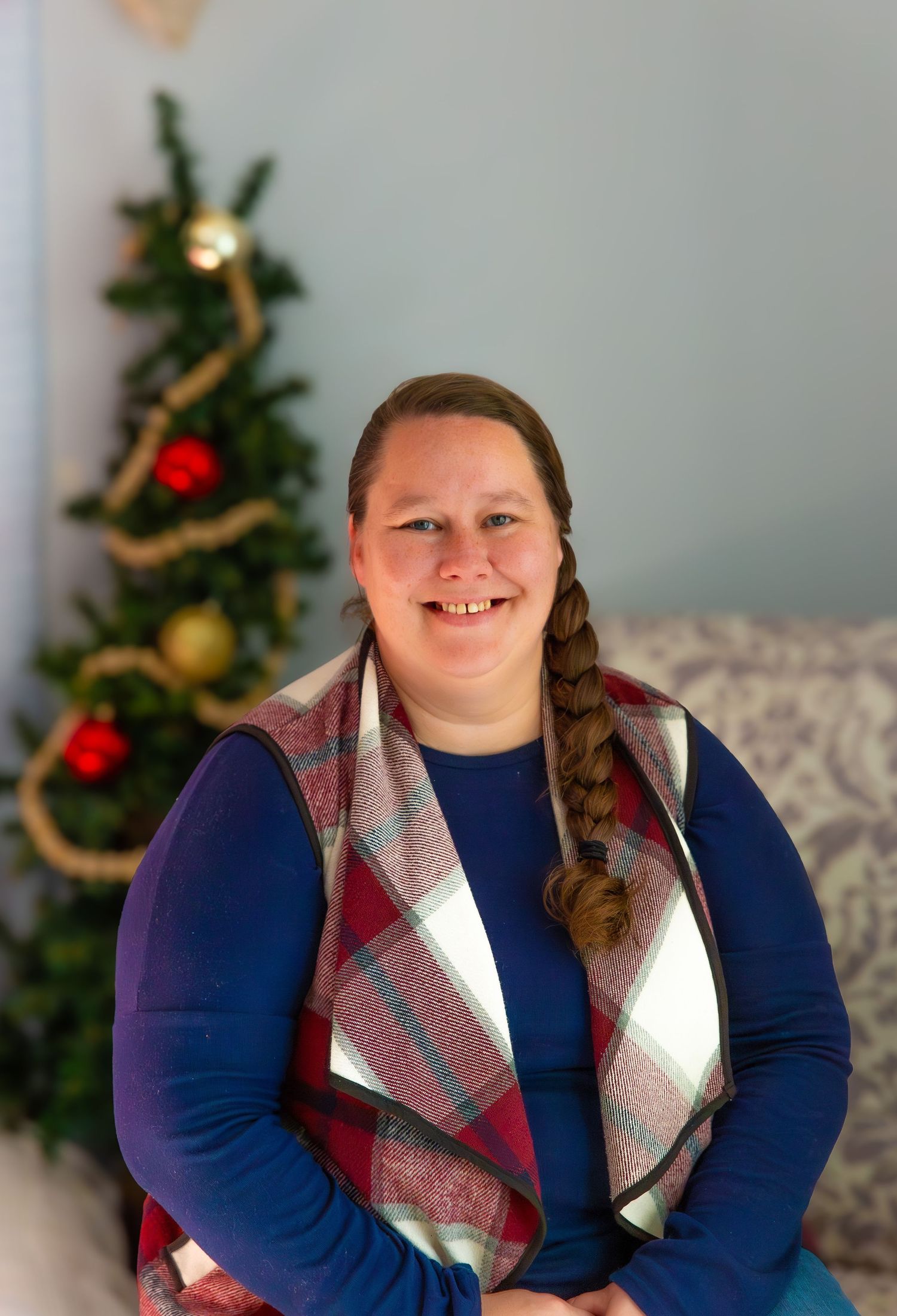 Holiday portrait with decorated Christmas tree and plaid vest against blue background.