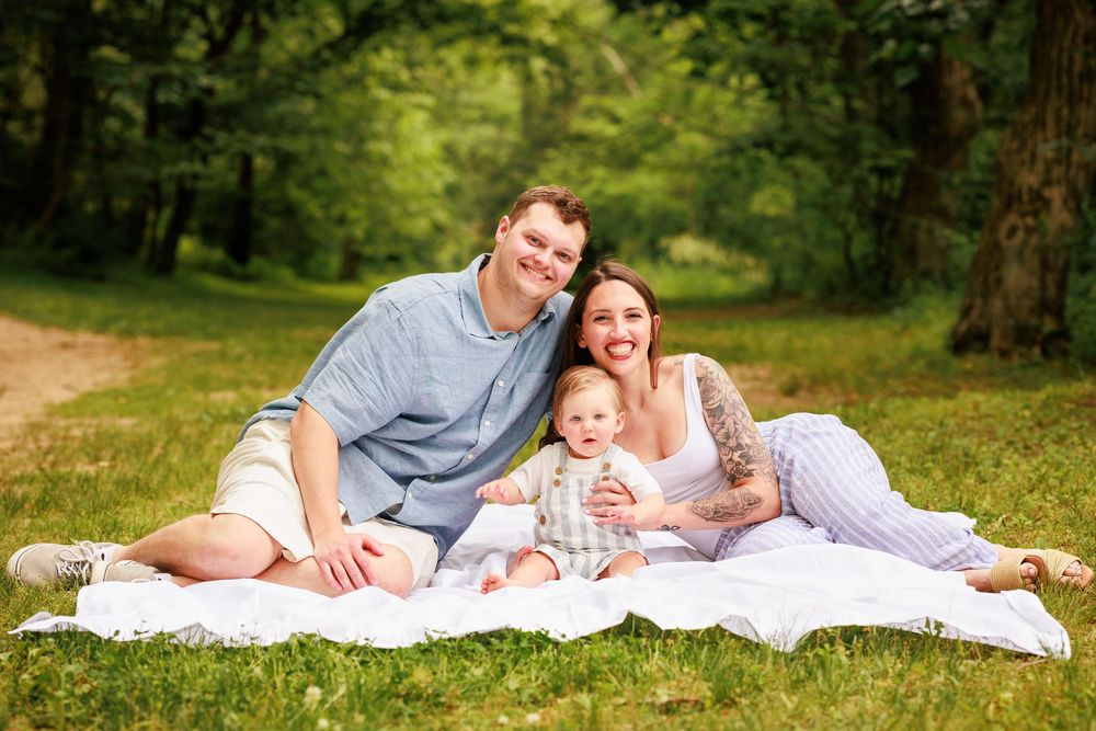Happy family with parents and baby sitting on a blanket in a lush green park for an outdoor photo.